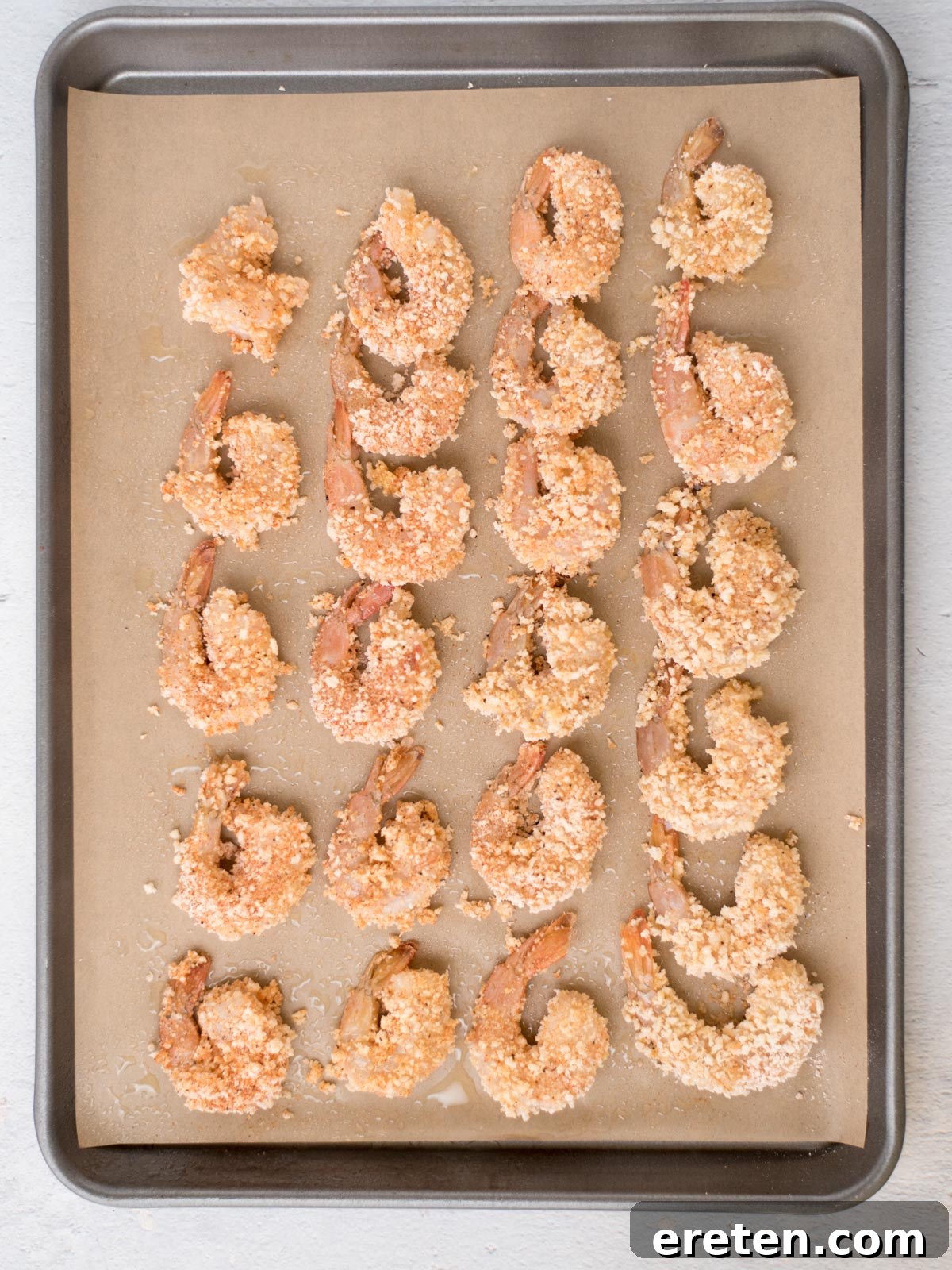 Crispy Baked Bang Bang Shrimp 6 Perfectly breaded shrimp laid out neatly on a parchment-lined baking sheet, glistening lightly with oil, poised for their journey into the oven to become crispy.