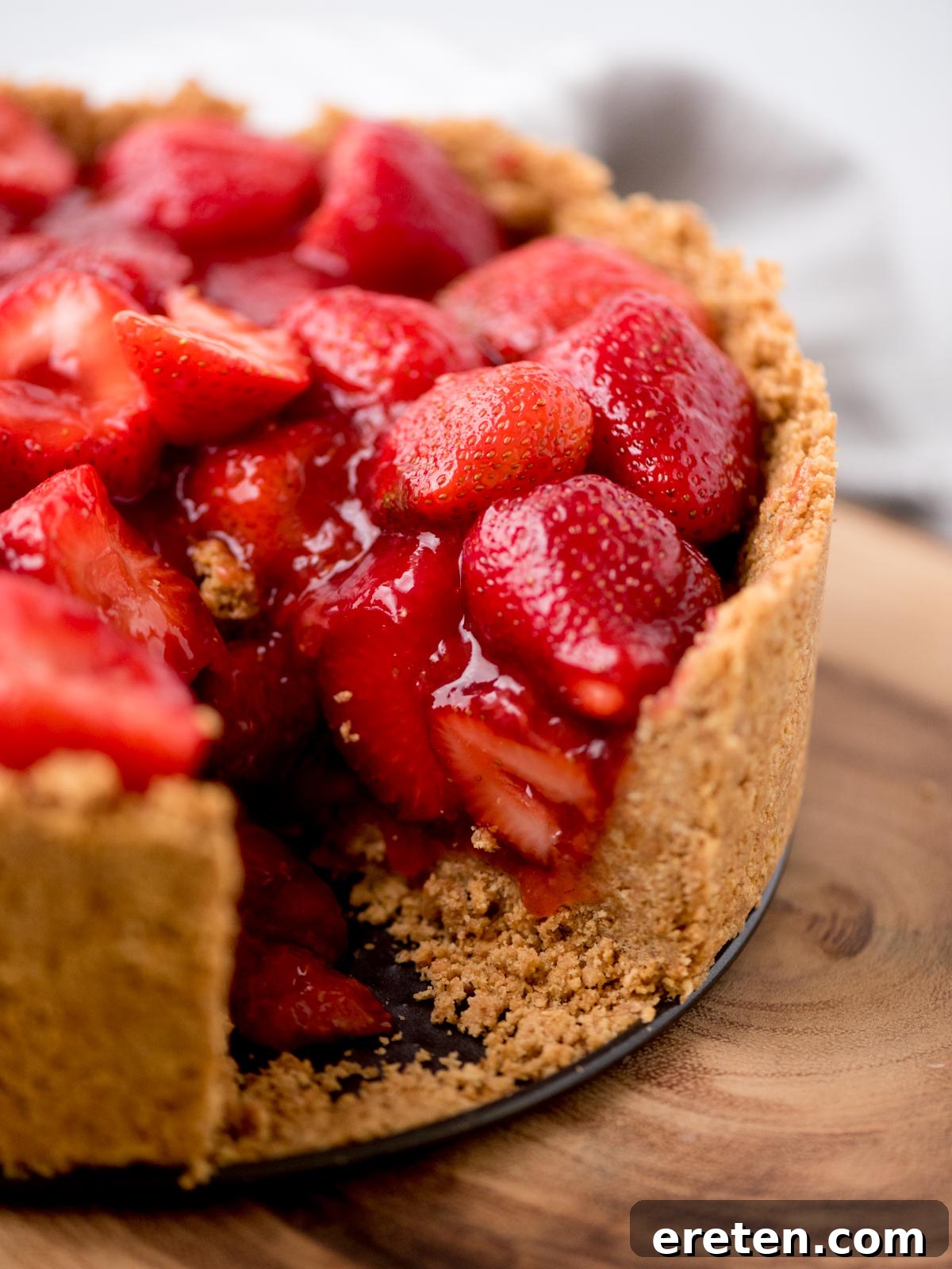 A whole no-bake strawberry pie with one slice removed, revealing the generous, luscious strawberry filling and crunchy graham cracker crust.