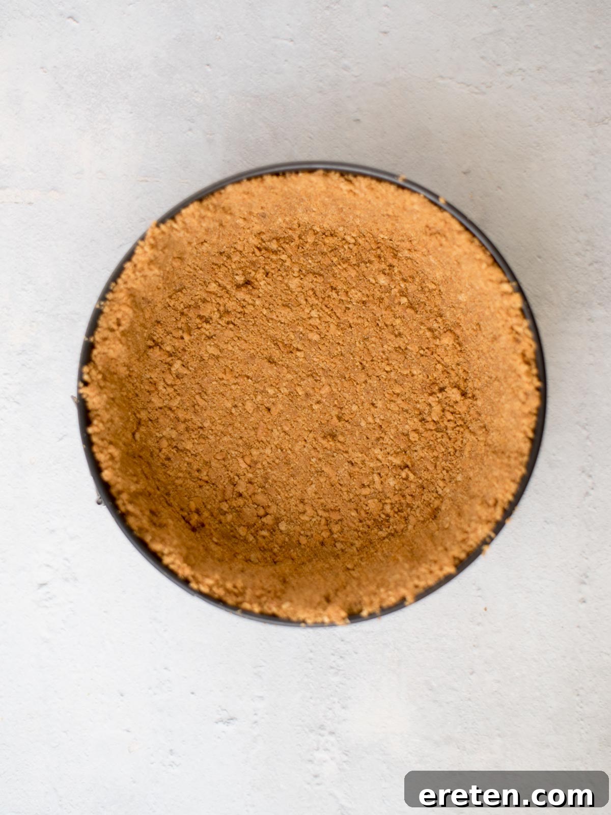 A golden graham cracker crust perfectly pressed into a springform pan, ready for the strawberry filling.
