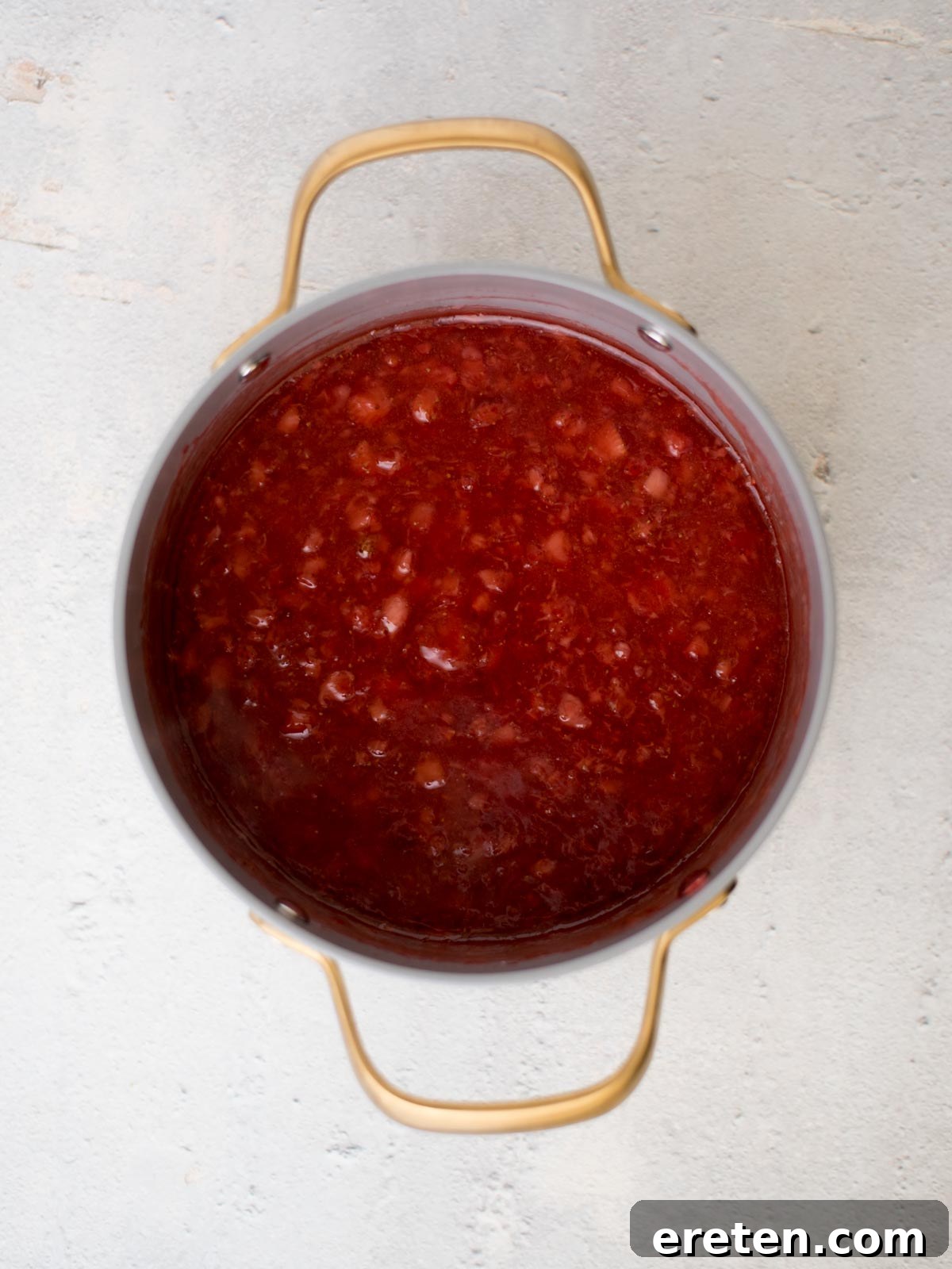Strawberry jam filling simmering in a saucepan on the stove, showing its thickening consistency.