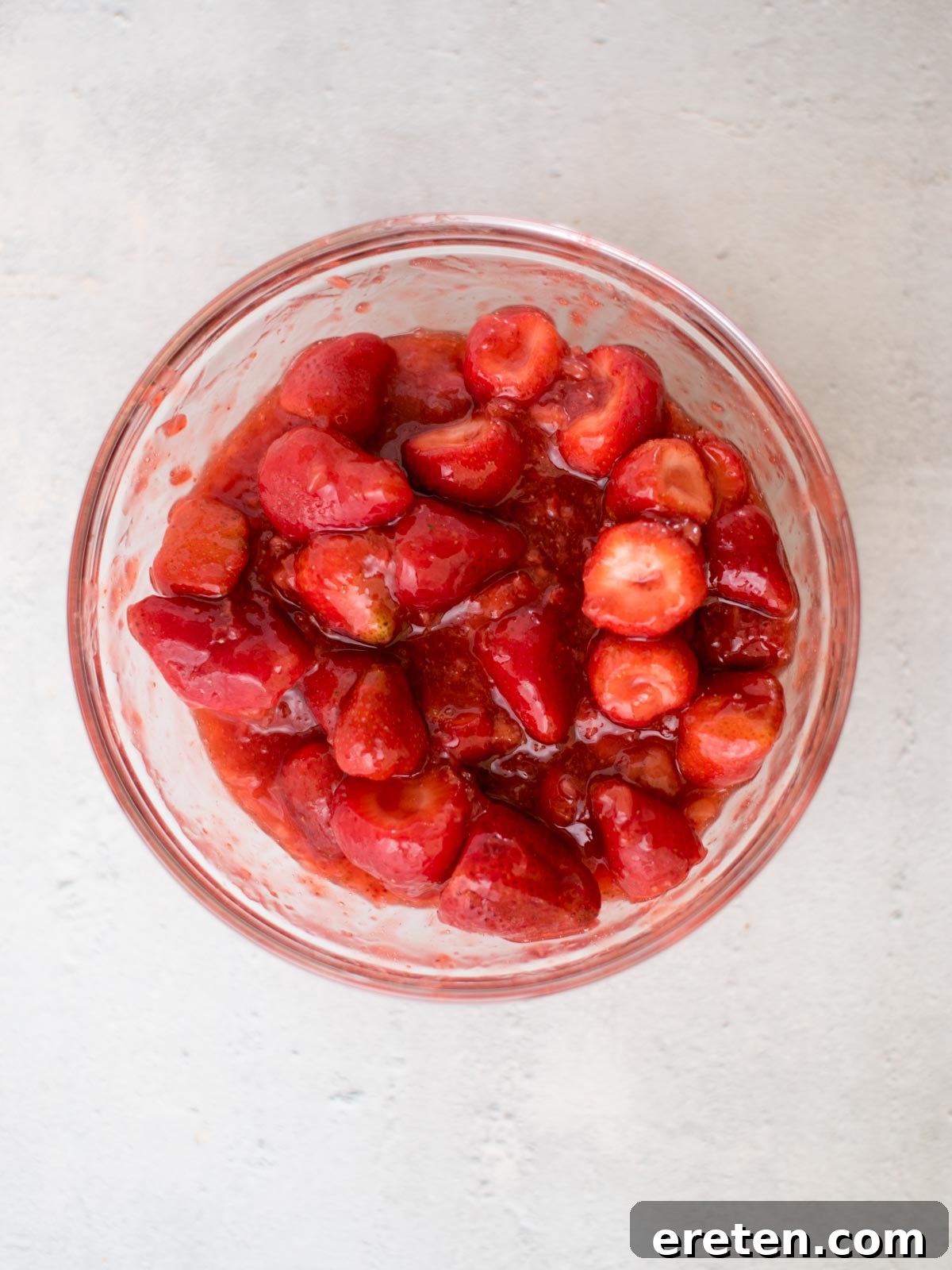 Fresh strawberry slices being mixed with the cooled jam filling in a large glass mixing bowl.