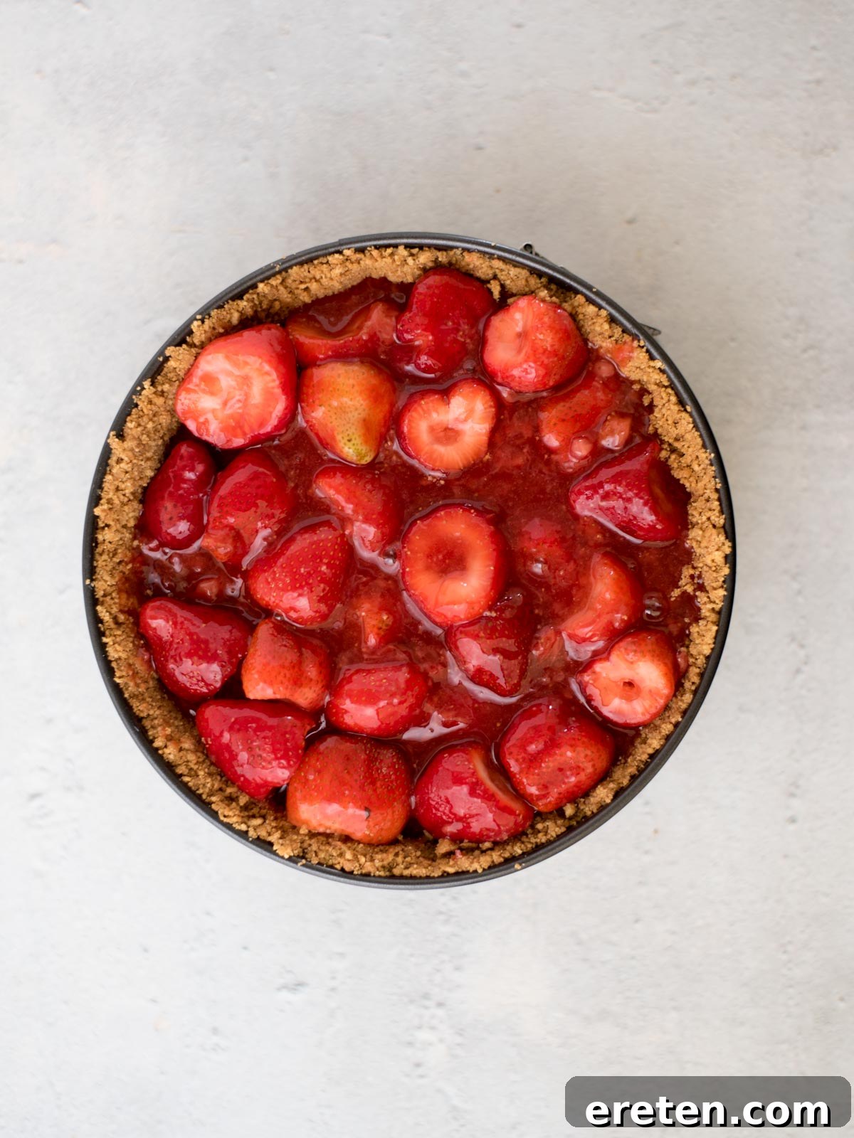 The fully assembled strawberry pie filling poured into the graham cracker crust within a springform pan, ready for chilling.