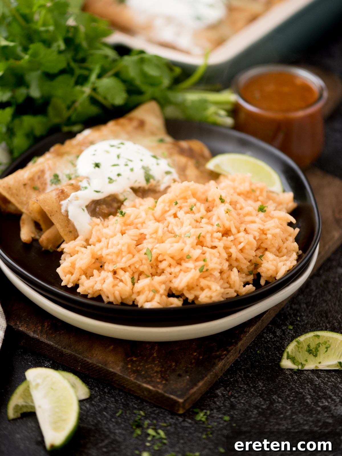 Spanish rice on a plate with enchiladas topped with chopped cilantro on a wooden board