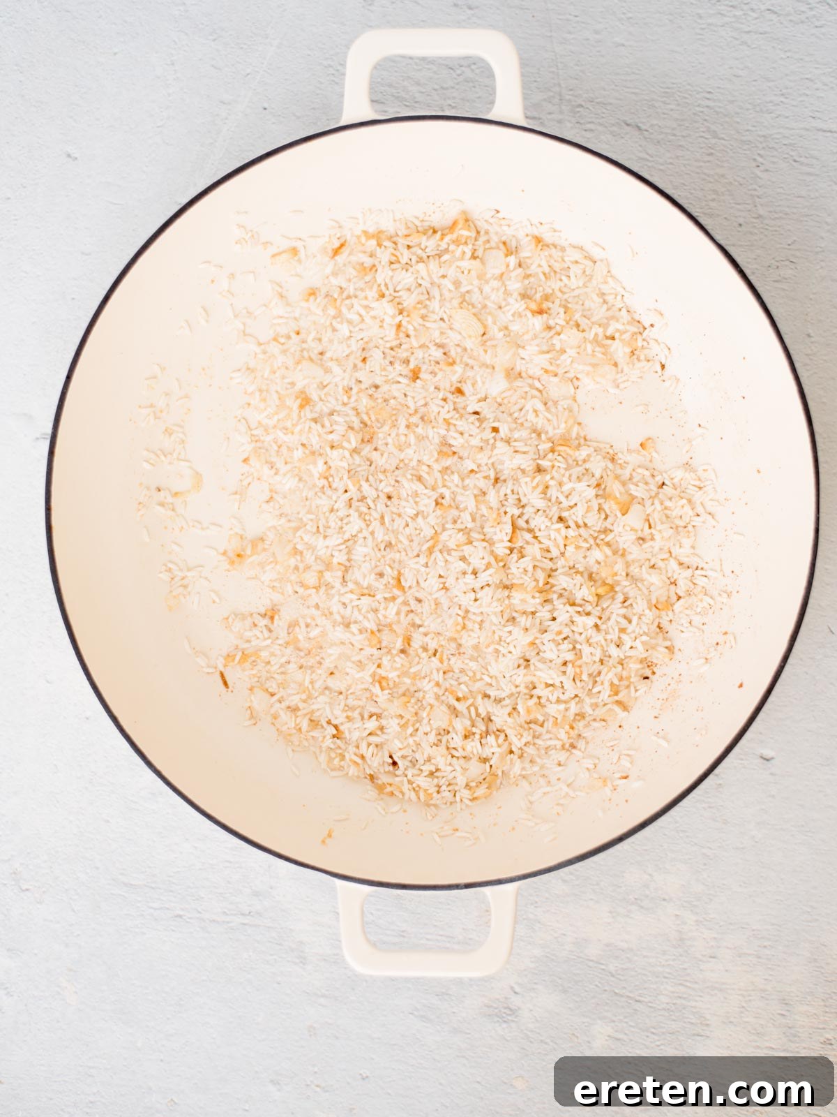 Rice toasting with oil, onion, and garlic powder in a white skillet