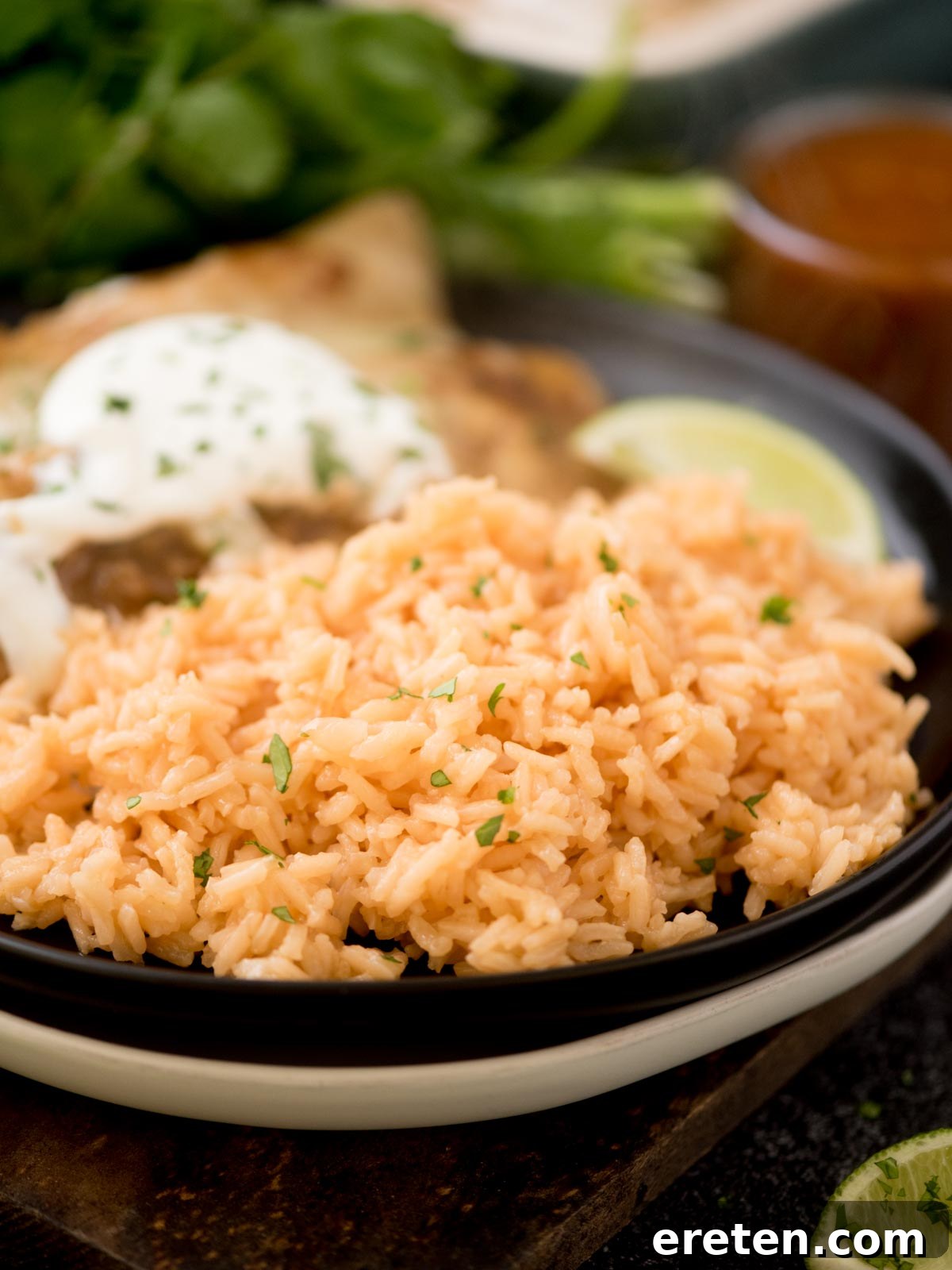 Spanish rice on a plate with enchiladas topped with chopped cilantro on a wooden board
