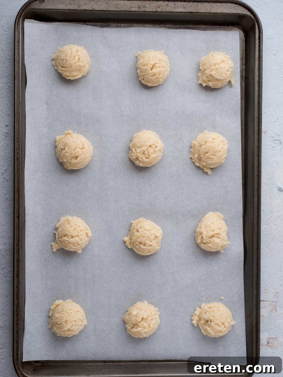 Twelve dough balls, perfect for the best Amish sugar cookies, are evenly spaced on a parchment-lined baking sheet, ready to be baked.