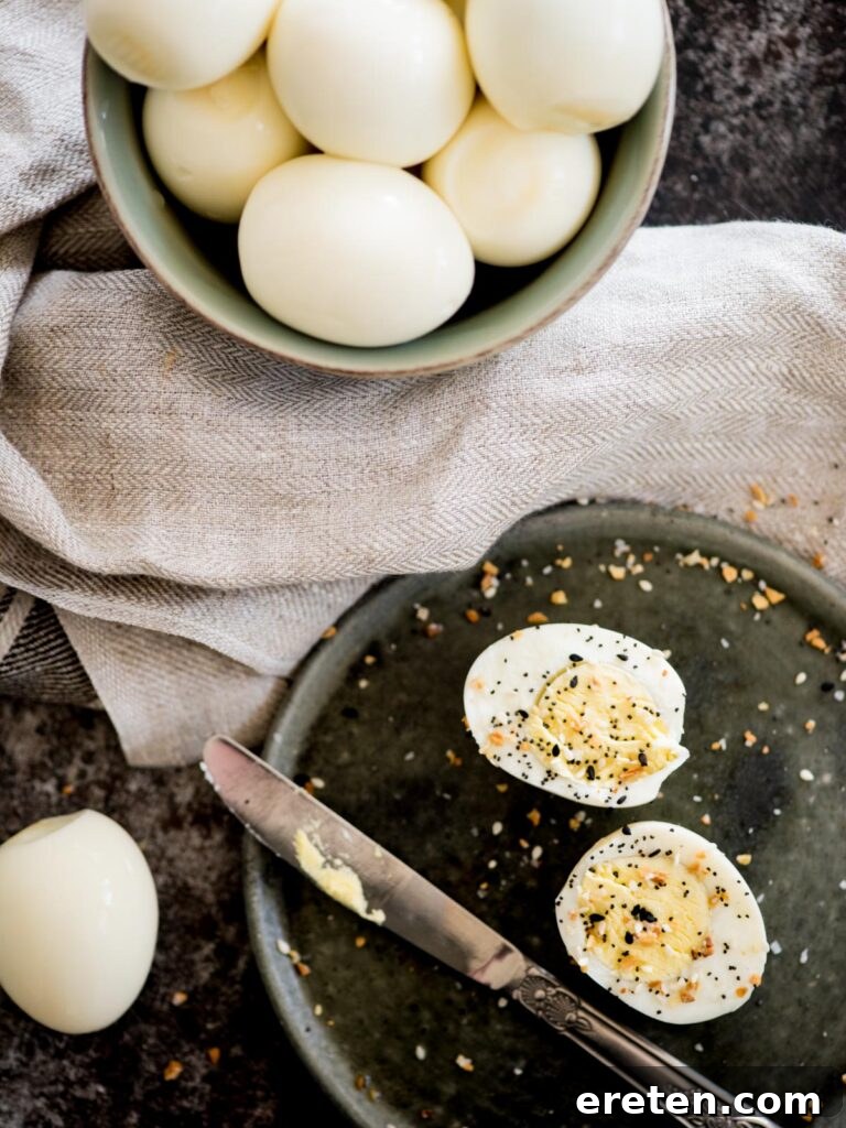Foolproof Hard Boiled Eggs in Instant Pot 8 A bowl full of perfectly hard-boiled Instant Pot eggs, with one sliced egg on a plate seasoned generously with everything bagel seasoning.