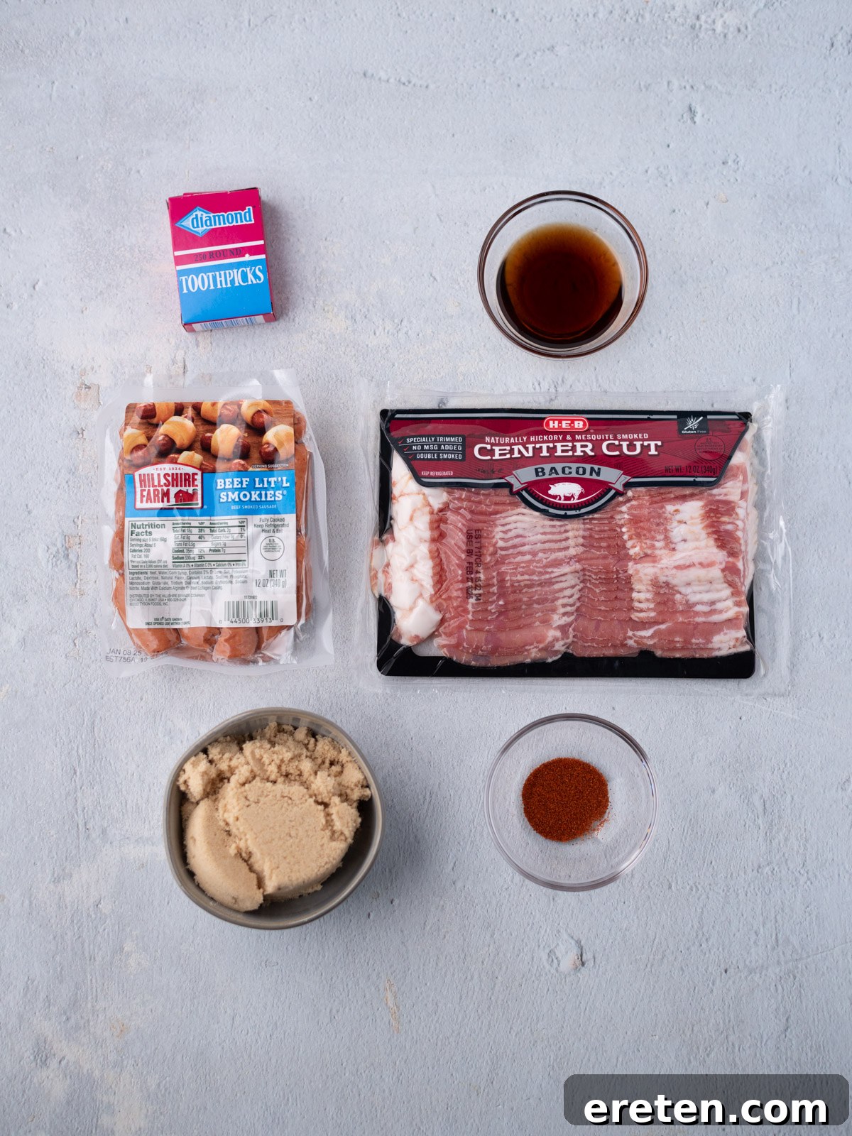 Golden Glazed Bacon Bites 3 Five ingredients and toothpicks arranged on a light surface: a pack of beef little smokies, center cut bacon, brown sugar in a bowl, cayenne in a small bowl, a bowl of maple syrup, and a box of toothpicks.