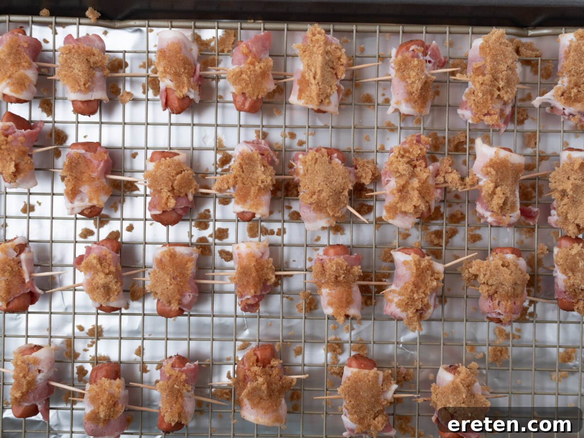Golden Glazed Bacon Bites 5 Raw bacon-wrapped bites on a wire rack, topped with brown sugar, arranged in rows and secured with toothpicks, ready for baking on a foil-lined baking sheet.