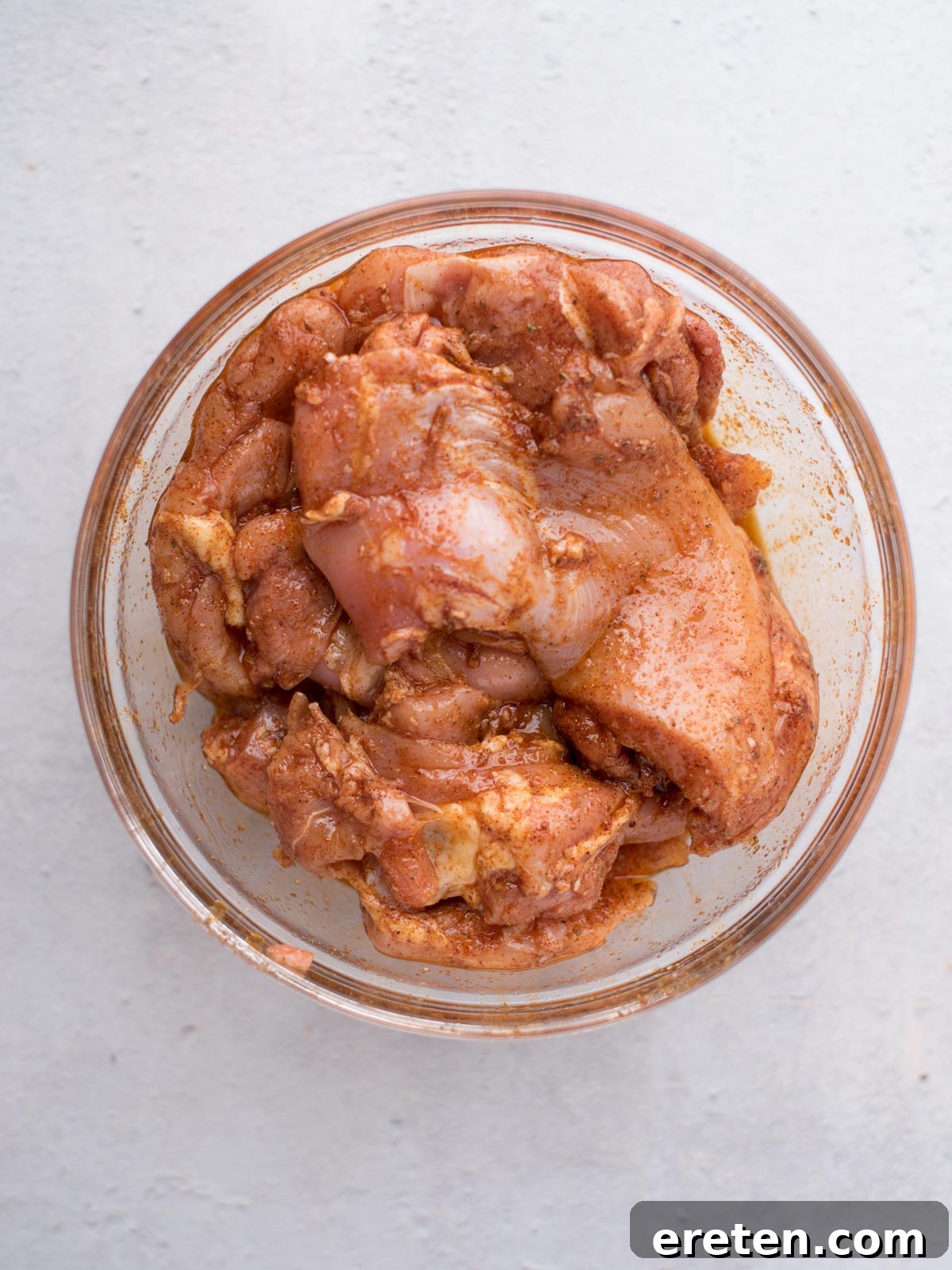 A glass bowl filled with raw chicken pieces coated in a reddish-brown marinade, perfect for making easy chicken fajitas, sits on a light-colored surface.