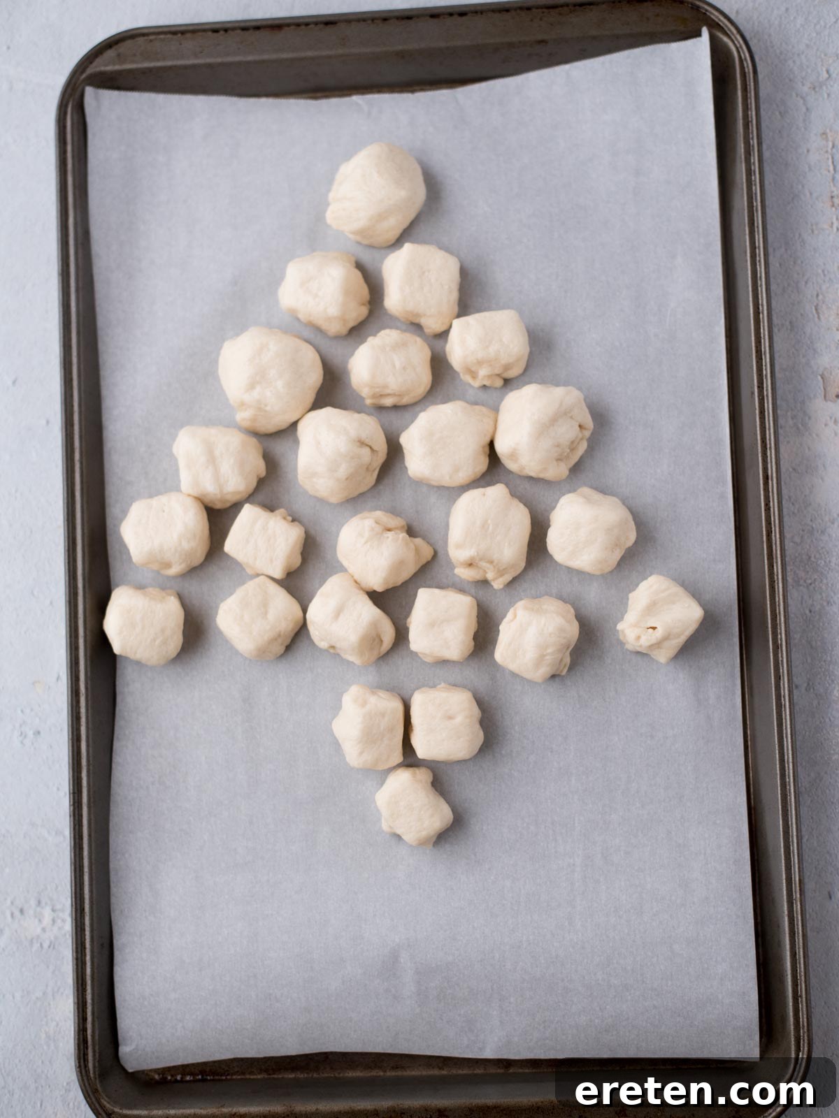 Small pieces of dough are arranged in the shape of a Christmas tree on a baking tray lined with parchment paper.
