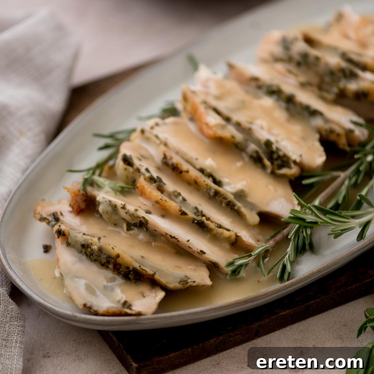 Sliced herb-crusted turkey breast topped with rich turkey gravy with drippings, arranged neatly on an oval plate and garnished with sprigs of fresh rosemary.
