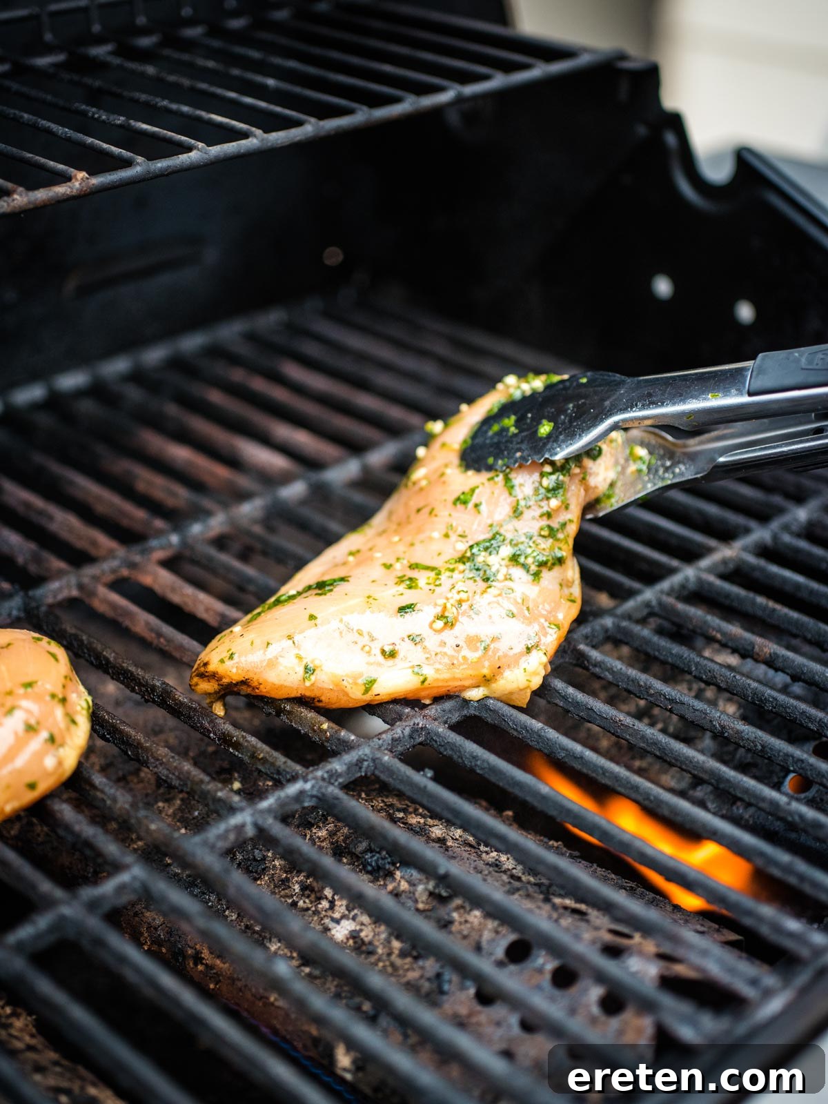 Raw marinated chicken being carefully placed onto a hot grill.