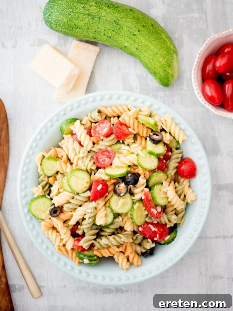 Vibrant Zesty Italian Pasta Salad in a blue bowl, garnished with fresh Parmesan, crisp cucumber, and ripe tomatoes, perfect for summer potlucks