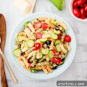 Appetizing Italian pasta salad in a serving bowl, surrounded by fresh parmesan, cucumber slices, and cherry tomatoes