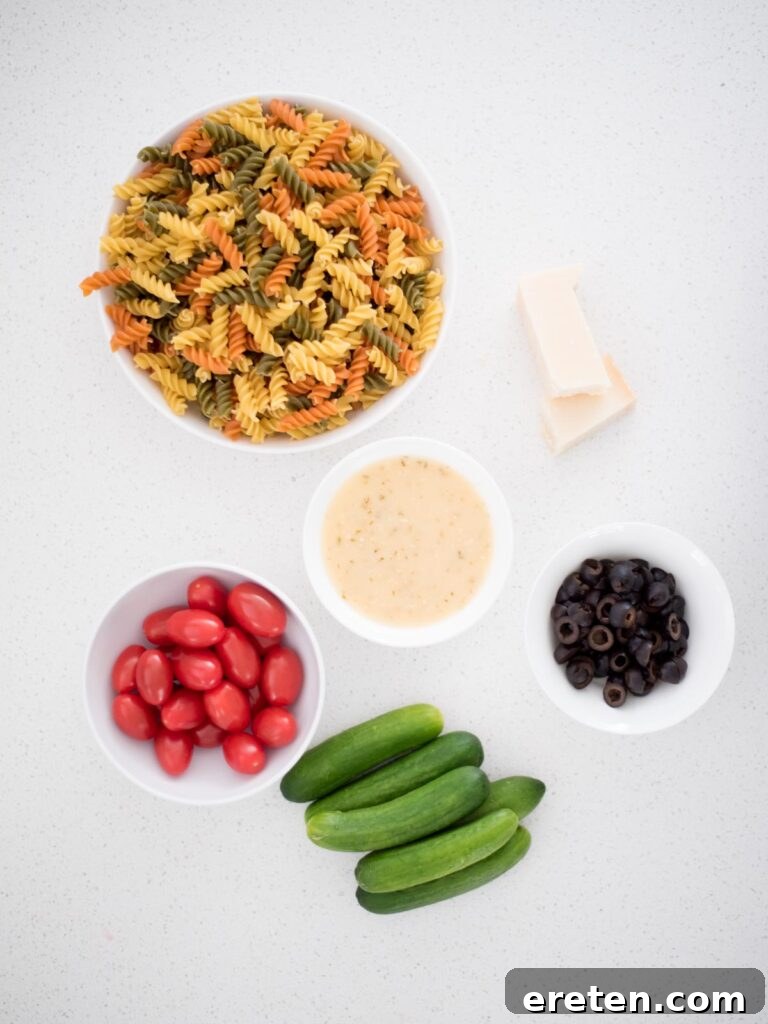 Fresh ingredients laid out for Zesty Italian Pasta Salad preparation, including pasta, olives, tomatoes, and cucumber
