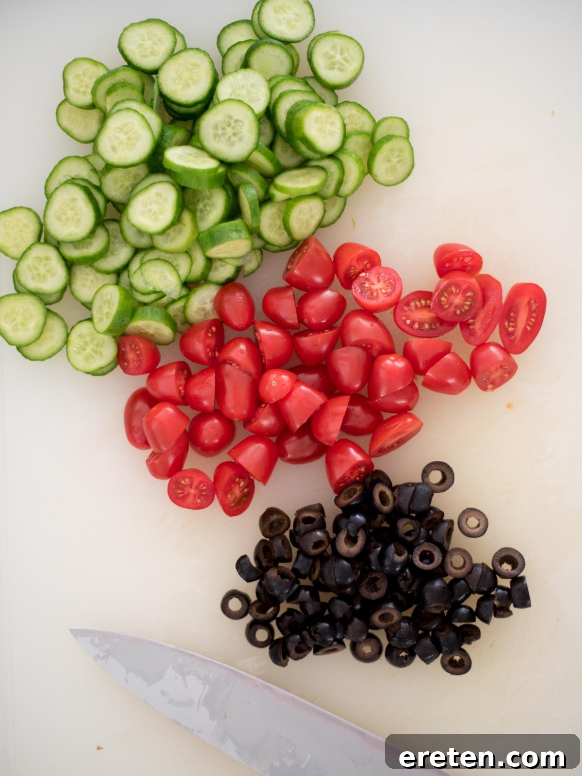 Freshly chopped English cucumber, black olives, and grape tomatoes on a cutting board, ready for a delicious Italian pasta salad