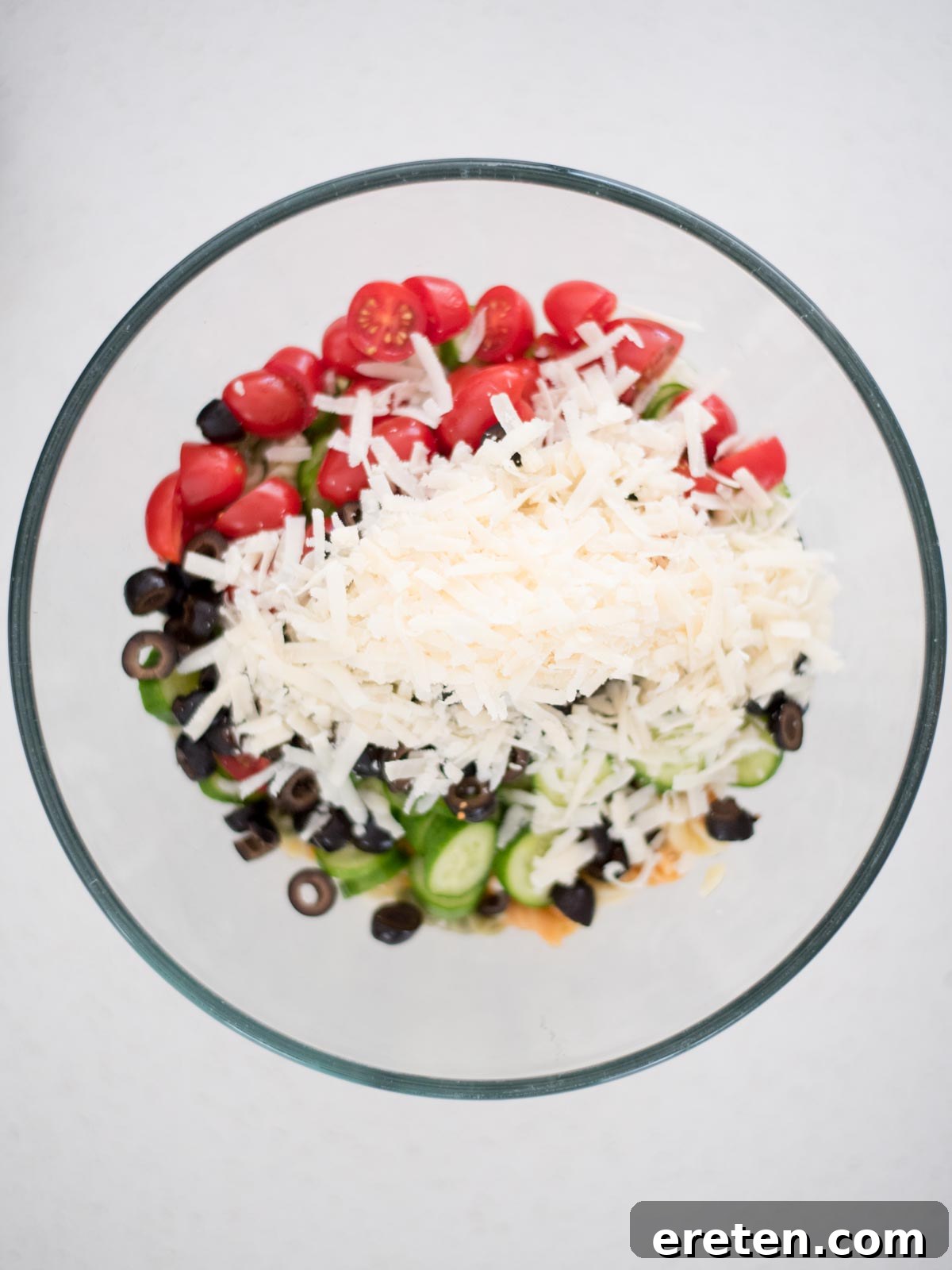 Shredded Parmesan cheese sprinkled over a mix of pasta, vegetables, and olives in a bowl, completing the Zesty Italian Pasta Salad