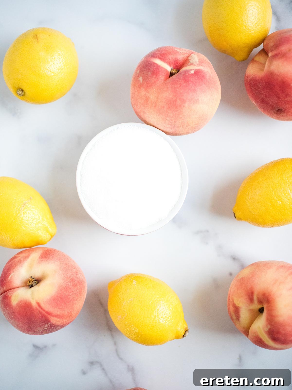 An overhead shot showcasing the fresh ingredients for peach lemonade: ripe peaches, bright lemons, and sugar.