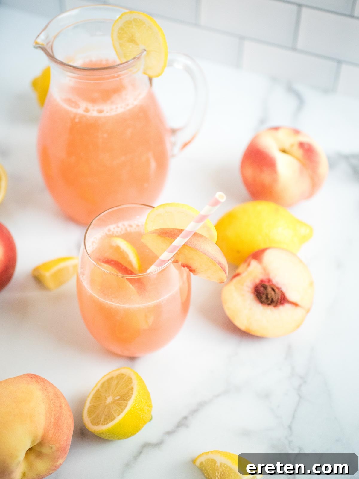 A beautiful arrangement featuring a glass of peach lemonade, surrounded by fresh lemons and peaches, with a large pitcher of the homemade drink in the background.