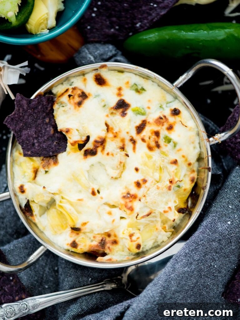 Spicy Artichoke Jalapeno Fusion 12 A freshly baked Jalapeno Artichoke Dip, golden and bubbly, served in a white baking dish with a wooden spoon.