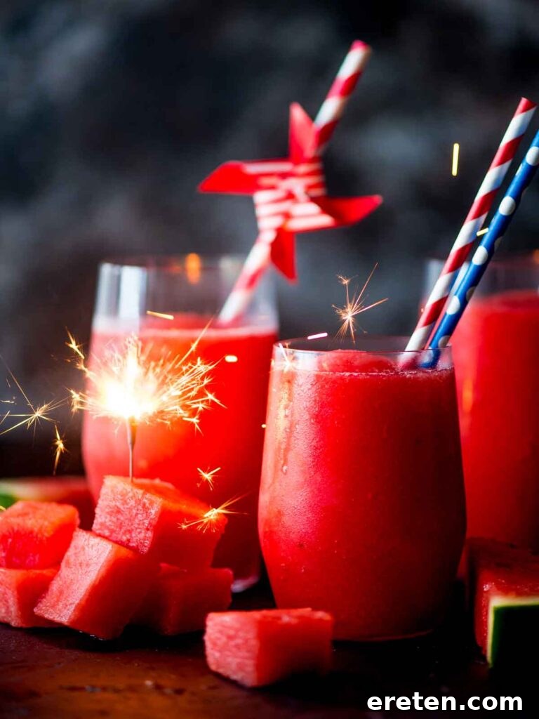 Two glasses of vibrant red watermelon slush with paper straws, garnished with frozen watermelon chunks. A sparkler is playfully inserted into a watermelon piece, capturing the essence of a summer celebration.