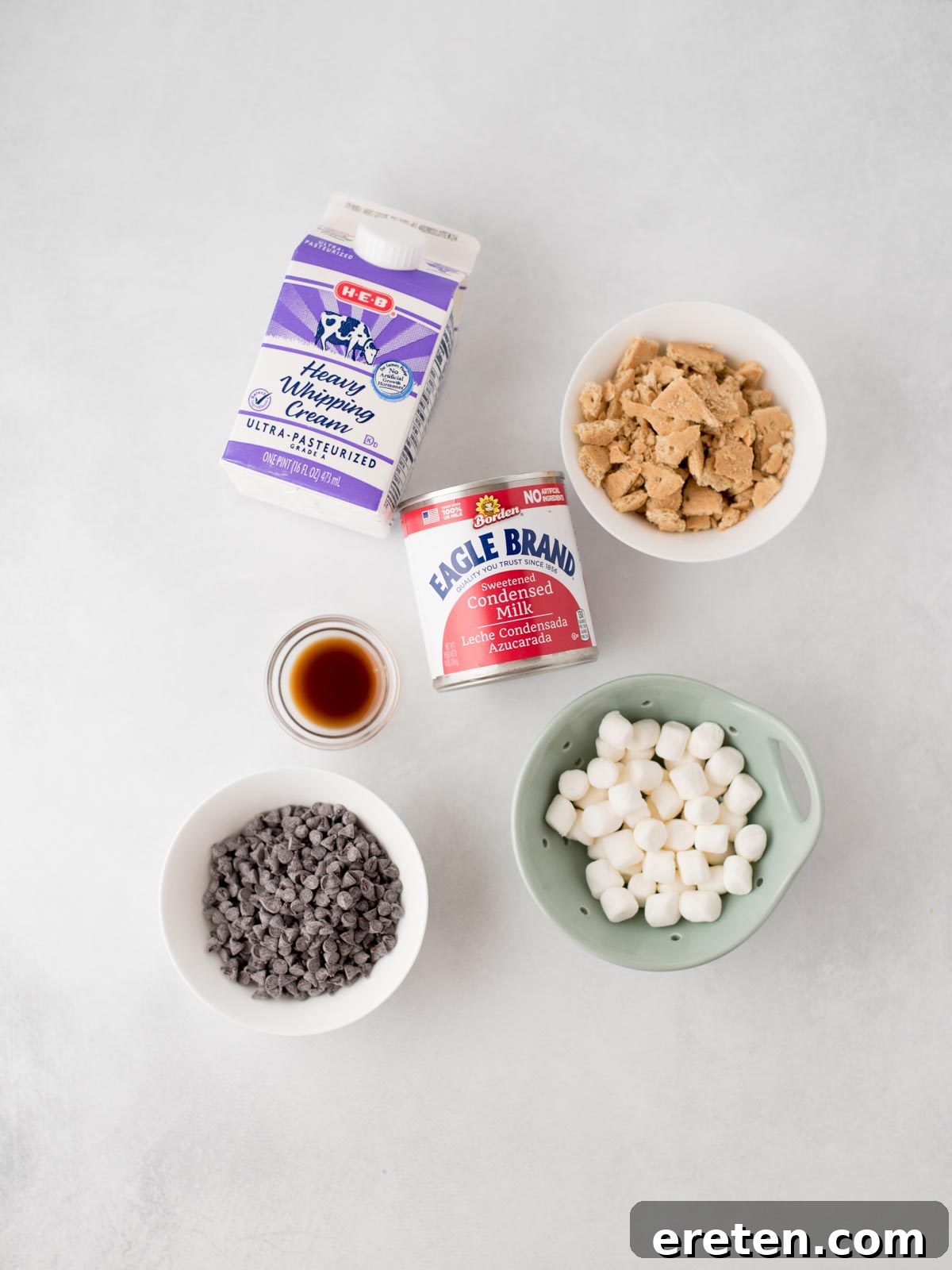Easy Homemade Smores Ice Cream 3 Five ingredients on a light surface: a carton of heavy whipping cream, a bowl of brown sugar, a can of condensed milk, a bowl of mini chocolate chips, a bowl of mini marshmallows, and a small cup of vanilla extract.