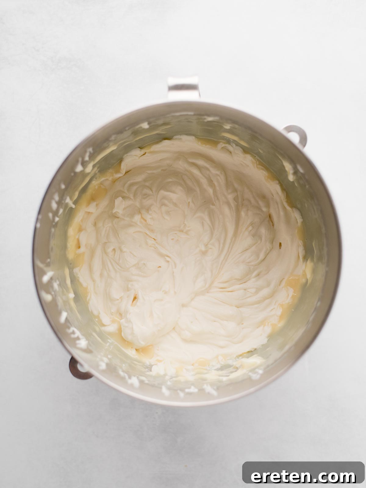 Easy Homemade Smores Ice Cream 5 A metal mixing bowl containing light, fluffy whipped cream against a white background.