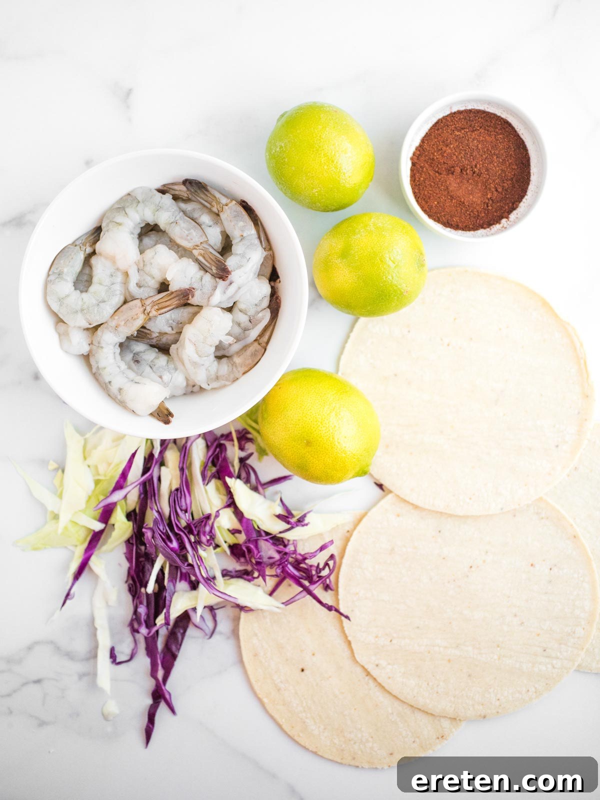 Ingredients laid out for chili lime shrimp tacos including shrimp, limes, spices, and cabbage