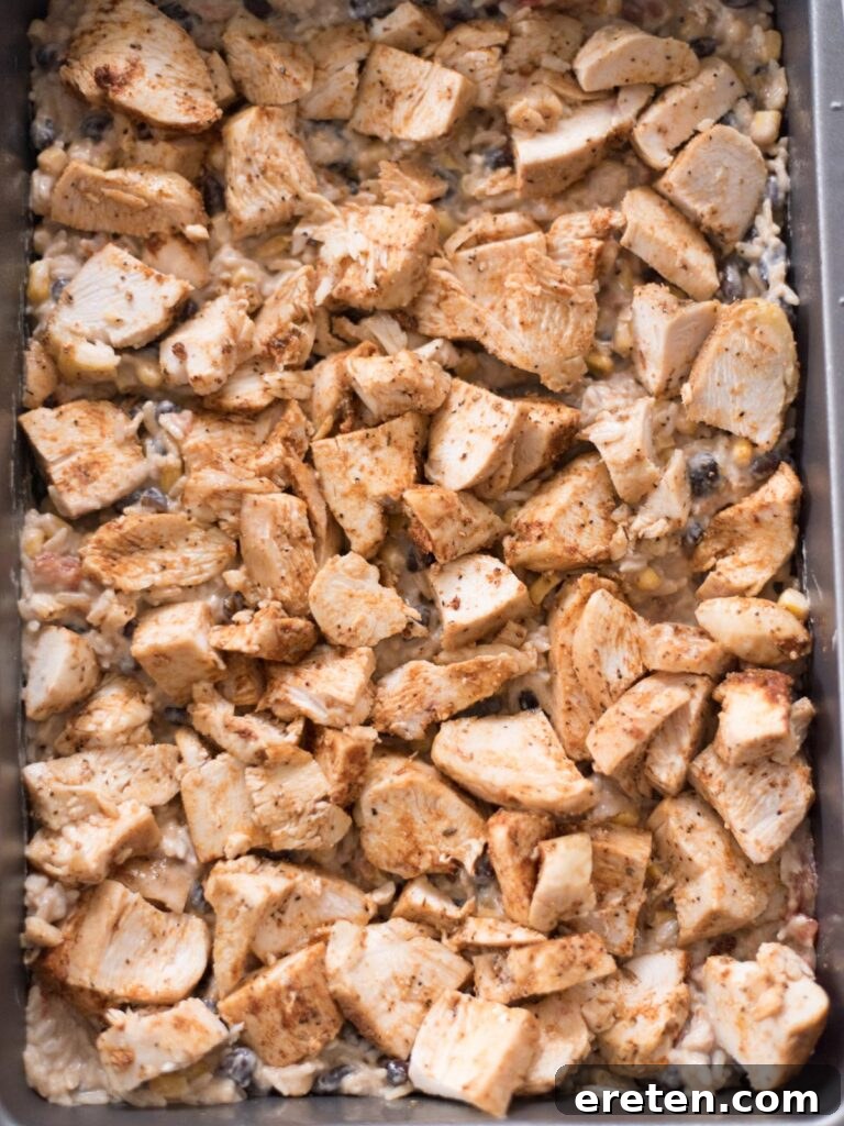Seasoned chicken added over the first rice layer in a baking dish, ready for the next layer.