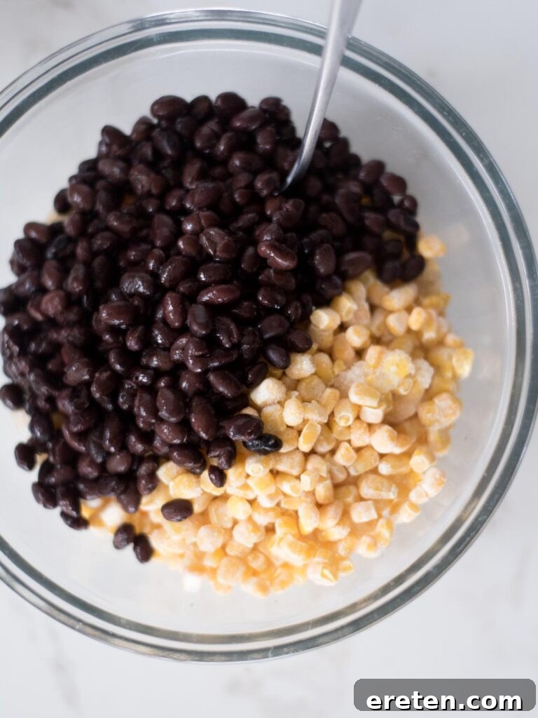 Black beans added over the corn and rice mixture in a mixing bowl, ready to be combined.
