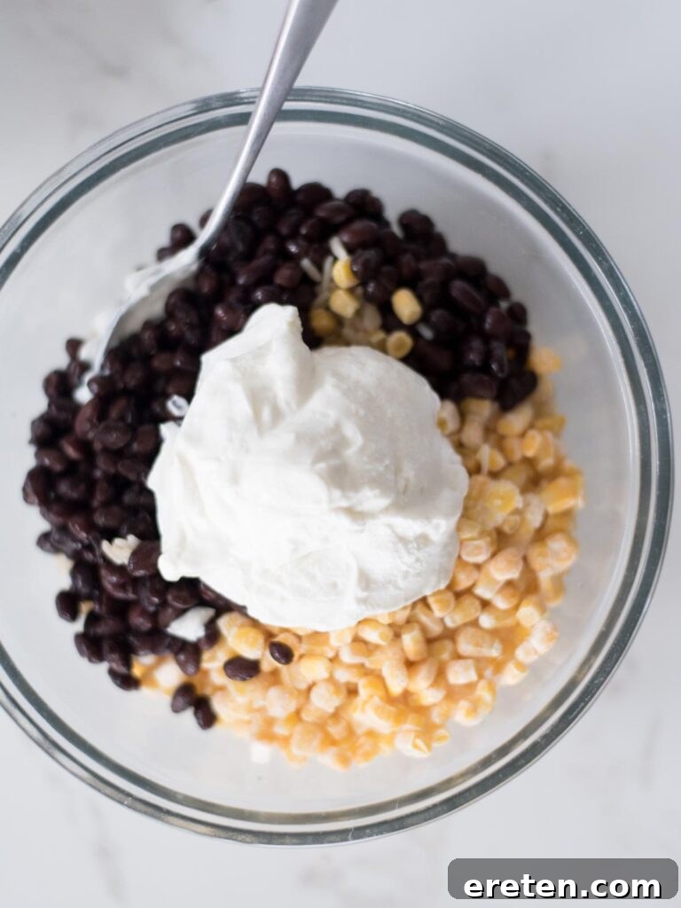 Sour cream added over the black beans, corn, and rice mixture in a mixing bowl.