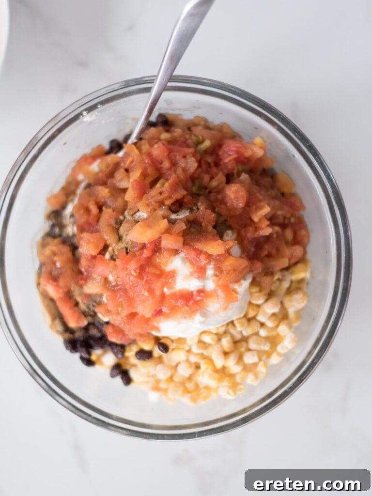 Diced tomatoes (Rotel) topping the corn, sour cream, and seasoning mixture in a mixing bowl, prior to mixing.