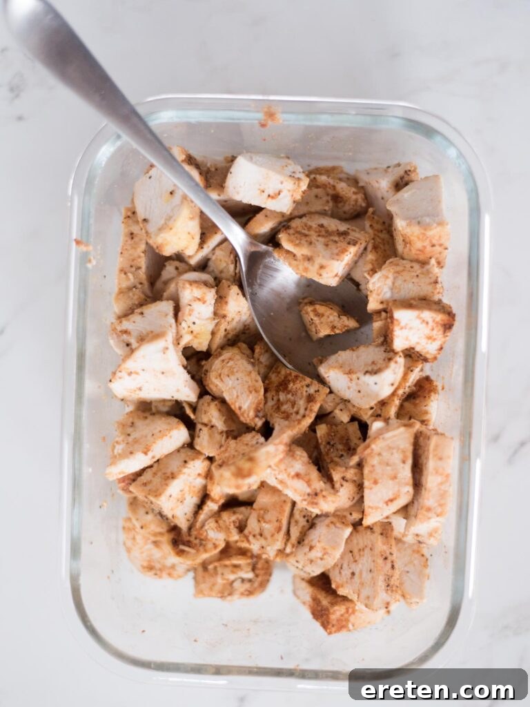 Shredded chicken coated with taco seasoning, combined in a bowl, showcasing its readiness for layering.