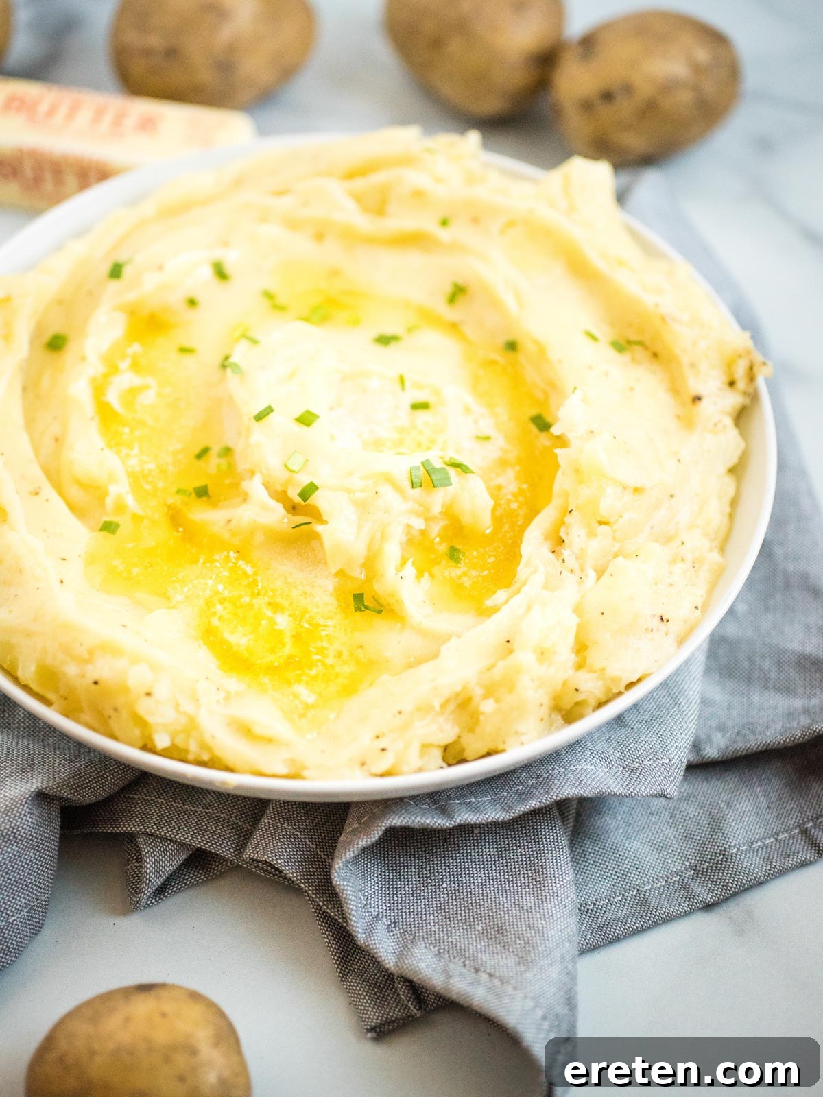 Creamy mashed potatoes in a white dish topped with melted butter and fresh chives