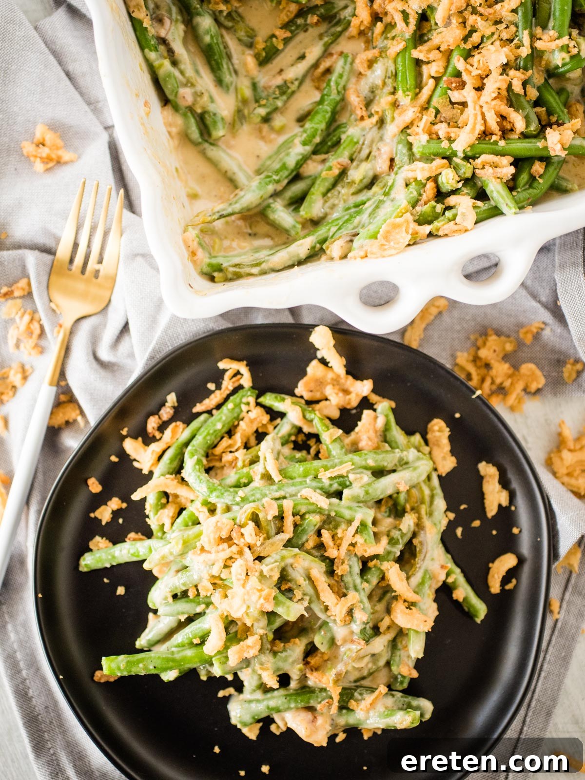 Ultimate Instant Pot Green Bean Casserole 8 a serving of green bean casserole on a black dish next to the serving dish full of casserole