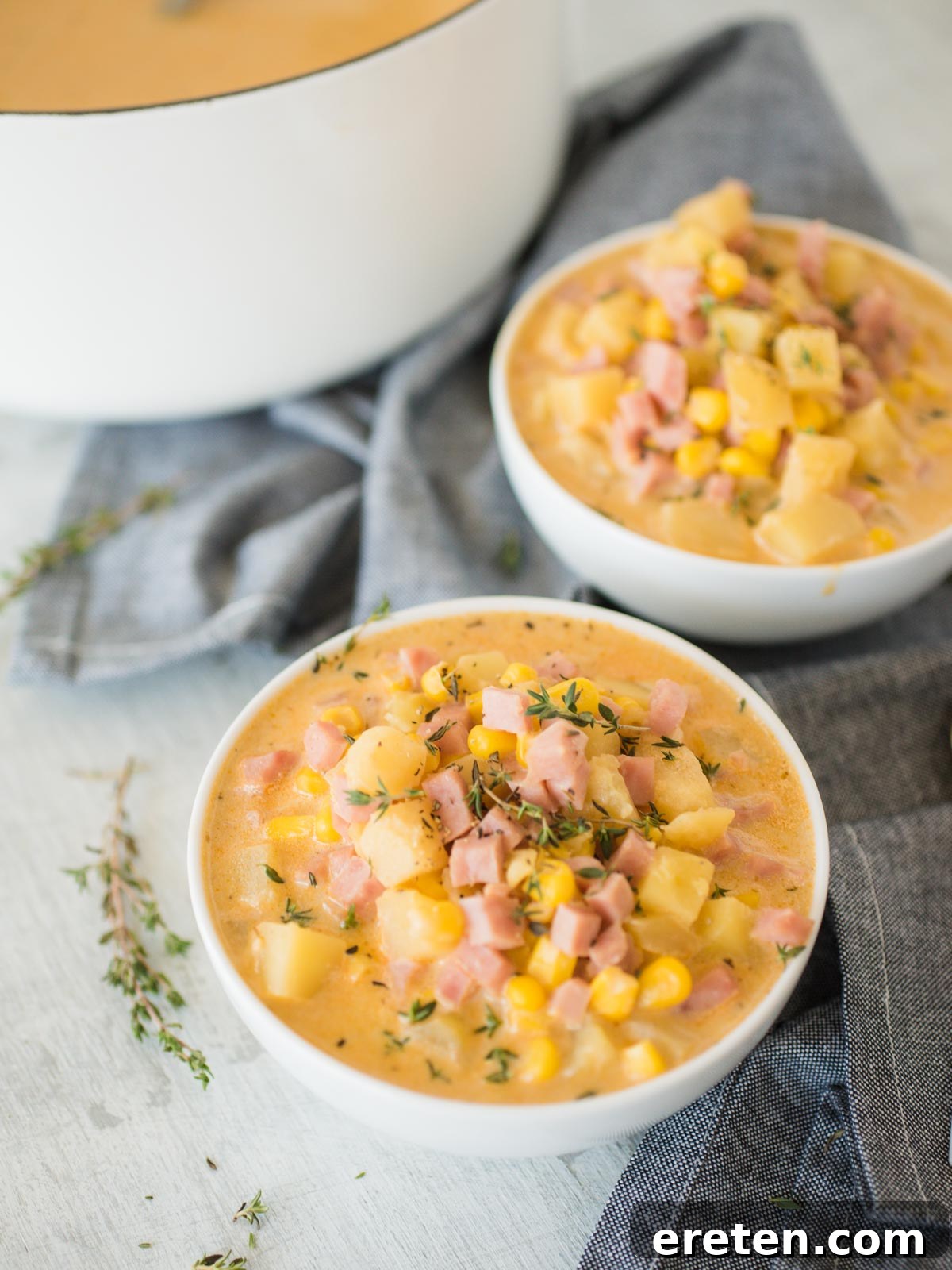 Two steaming bowls of creamy ham and potato corn chowder, garnished with fresh herbs.