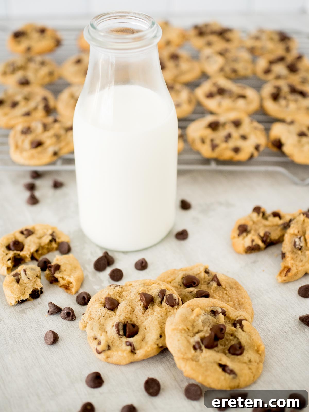 A stunning display of fresh chocolate chip cookies in front of a glass of milk and a rack of cooling cookies, a picture of homemade comfort