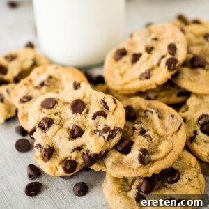 A stack of chocolate chip cookies in front of a glass of milk