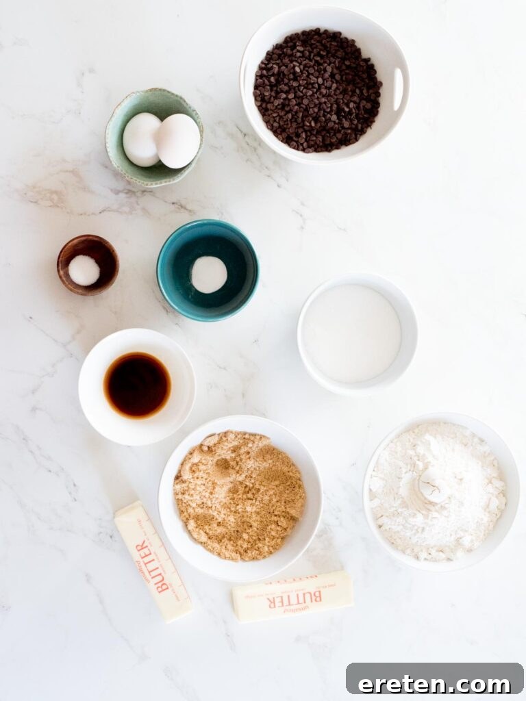 Neatly arranged ingredients to make soft chocolate chip cookies, including butter, sugars, eggs, flour, and chocolate chips