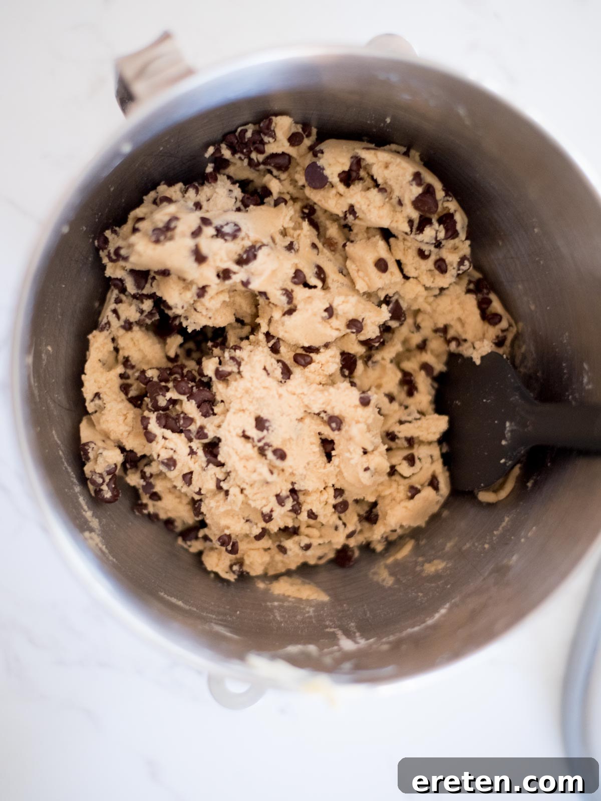 The best chewy chocolate chip cookie dough in a metal mixing bowl, brimming with chocolate chips