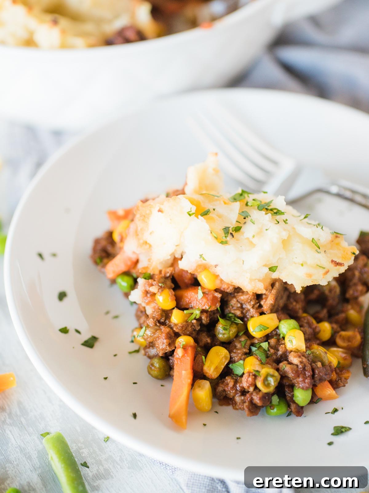 A close-up shot of a serving of Shepherd's Pie in a white shallow bowl, garnished with fresh herbs.