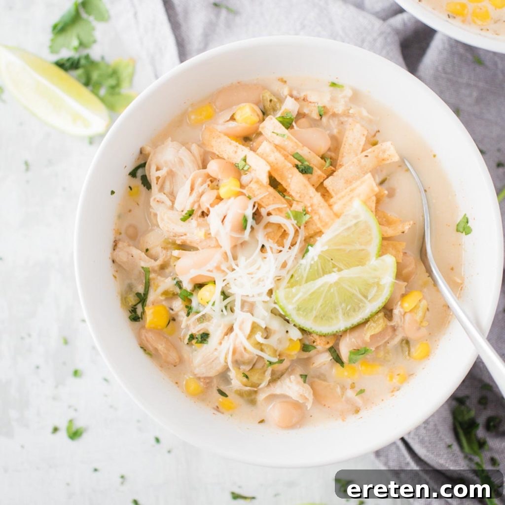 A simple white bowl filled with creamy white chicken chili, a spoon poised within, suggesting a comforting and delicious meal.