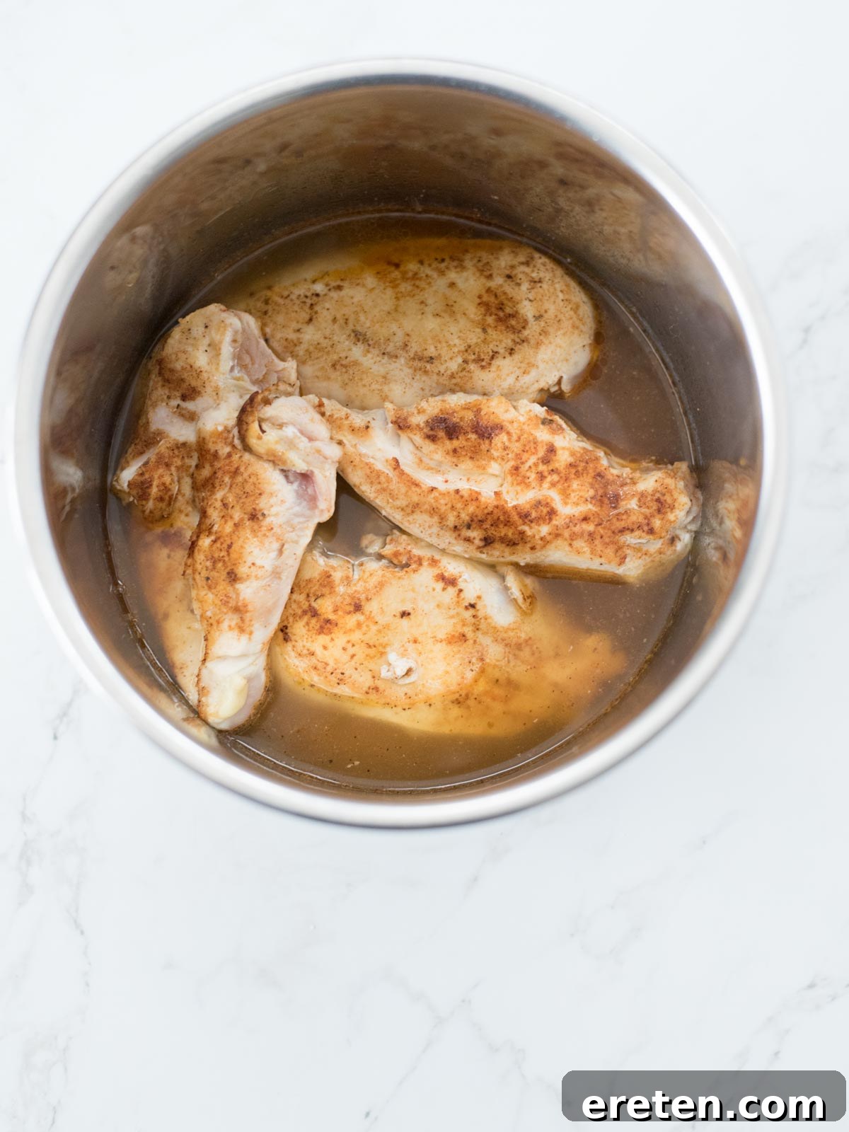 Chicken breasts covered with chicken broth and generously seasoned with taco spice, positioned inside the Instant Pot before pressure cooking.