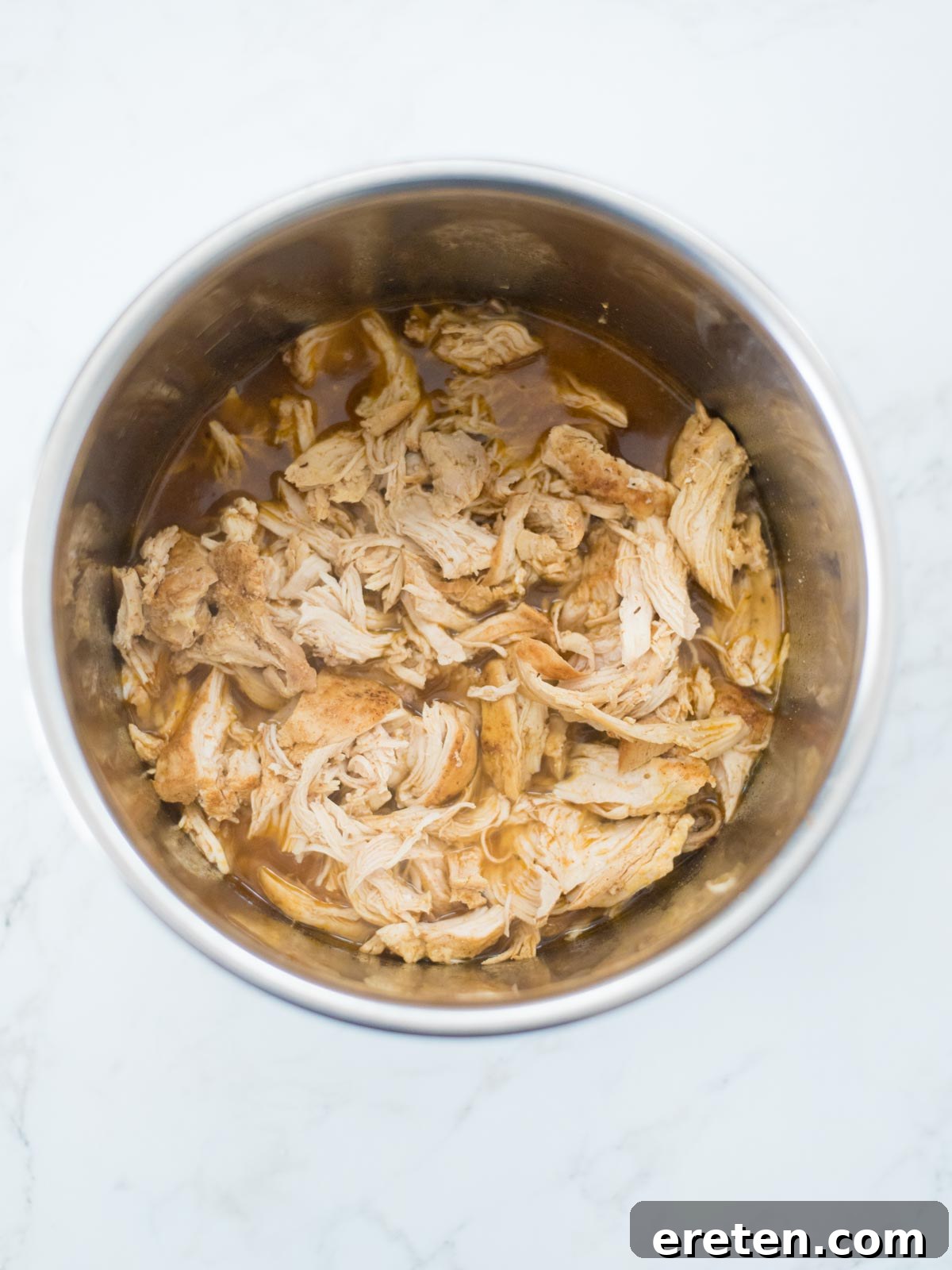 Tender, shredded chicken resting in its savory broth within the Instant Pot after being perfectly pressure cooked.