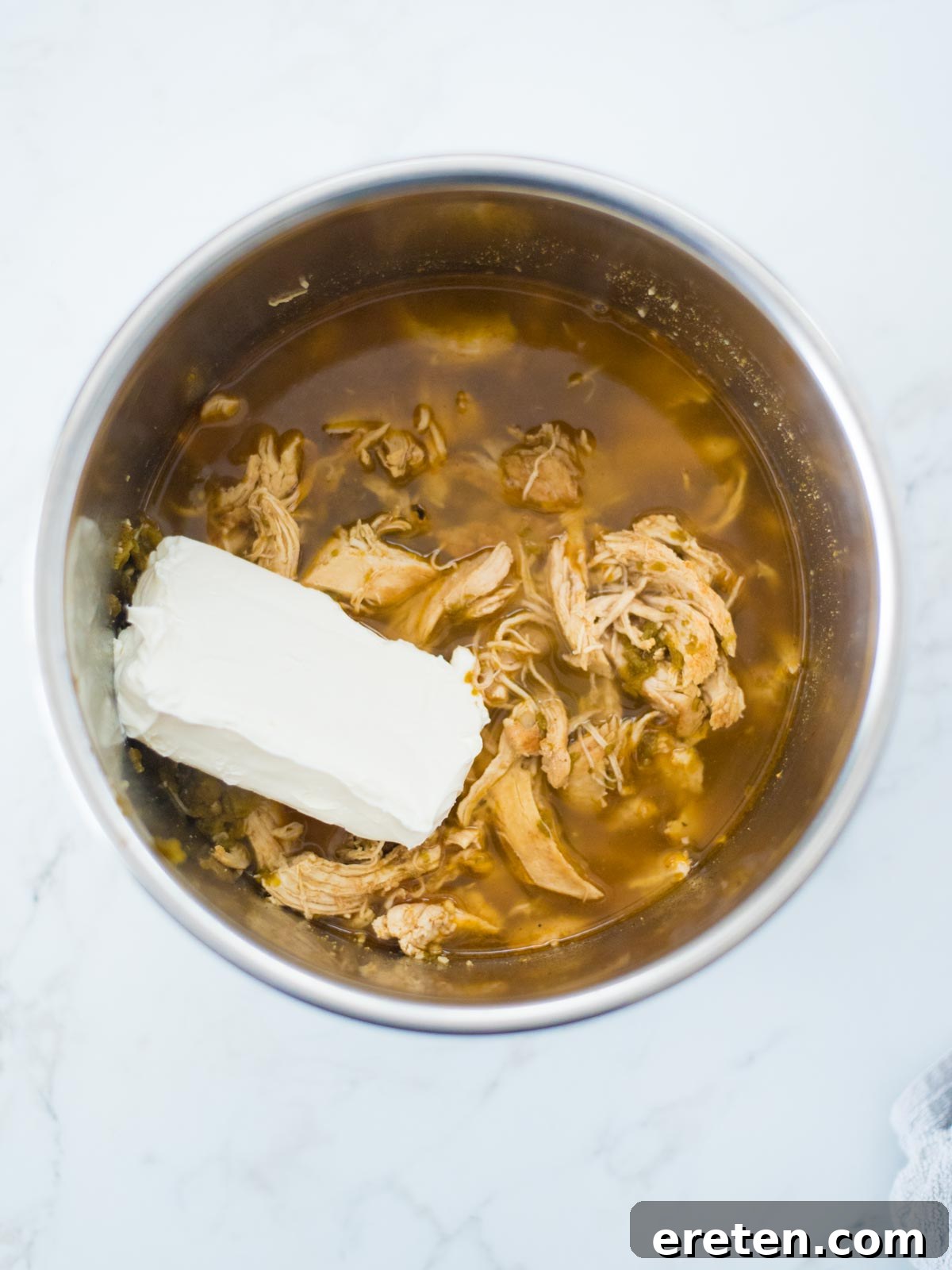 A block of cream cheese gently melting and dissolving into the chili mixture inside the Instant Pot, creating a smooth, creamy base.