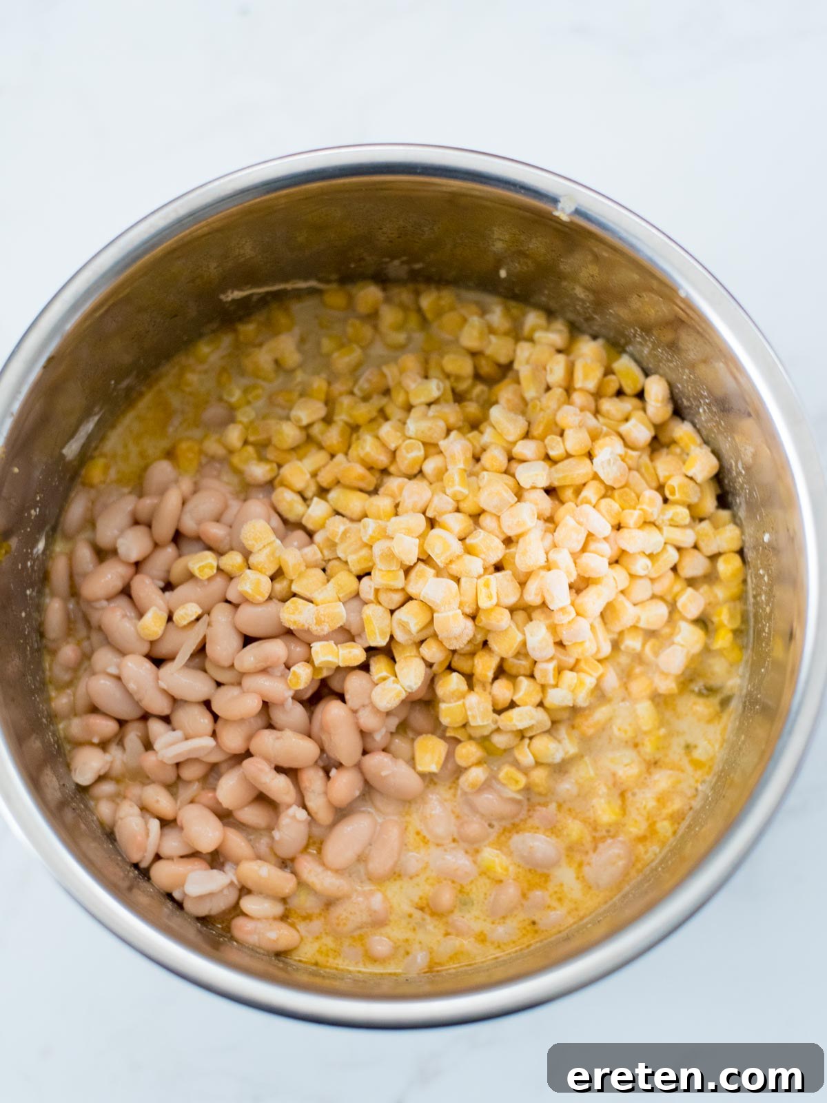 Sweet corn kernels and tender cannellini beans freshly added to the creamy white chicken chili, being stirred to combine all ingredients.