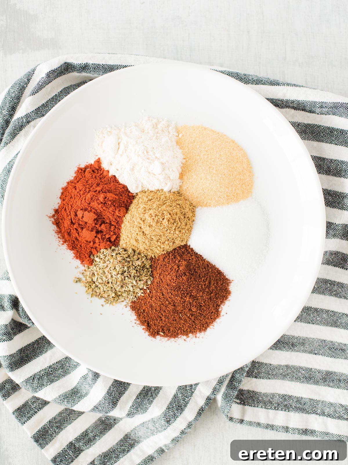 Homemade Mild Taco Spice Blend 3 Individual spices for taco seasoning laid out on a plate against a striped fabric background.