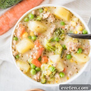 White bowl full of soup with a black spoon on a table with carrots and broccoli