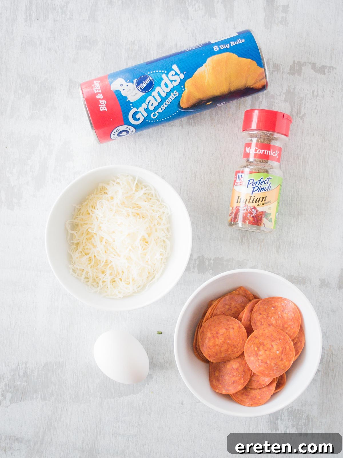 Collection of fresh ingredients for making pepperoni rolls, including crescent roll dough, pepperoni, shredded mozzarella, and Italian seasoning